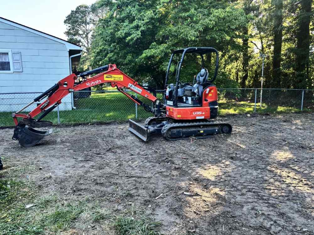 Red Kubota mini excavator parked on a dirt lot during residential site clearing and demolition preparation.