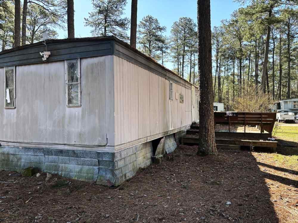 Older mobile home slated for residential teardown and site clearing in a wooded area.