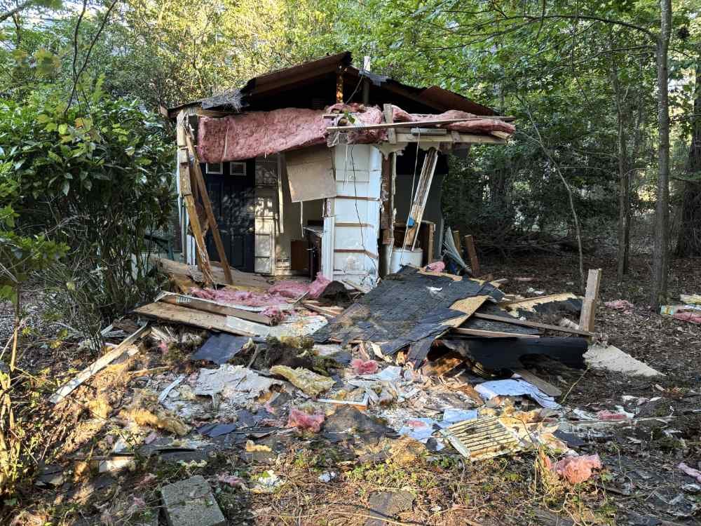 **Alt Text:**Partially demolished wooden shed with scattered building debris and exposed insulation during a residential teardown.