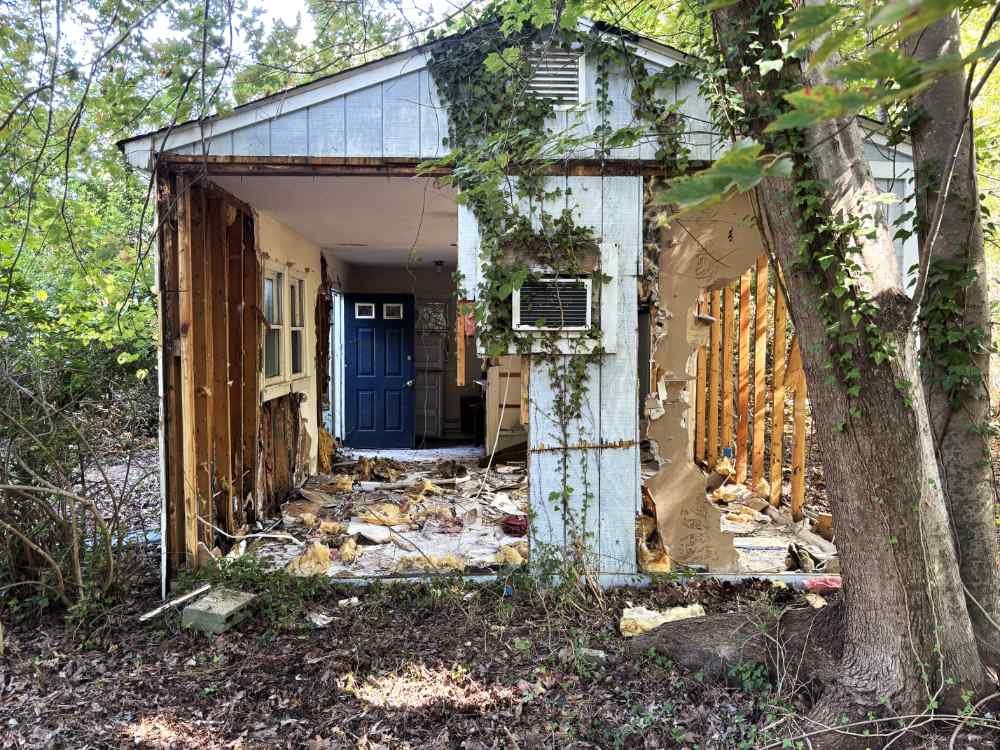 Partially demolished residential structure with exposed framing studs and debris during site clearing.