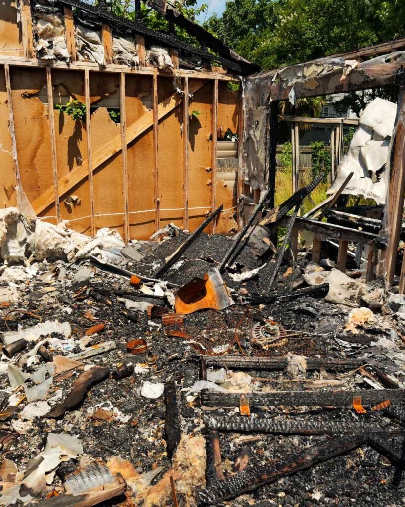 Charred structural framing and debris pile after fire damage awaiting site clearing and demolition.