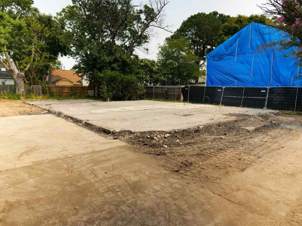 Cleared residential site with exposed concrete slab after structure demolition.