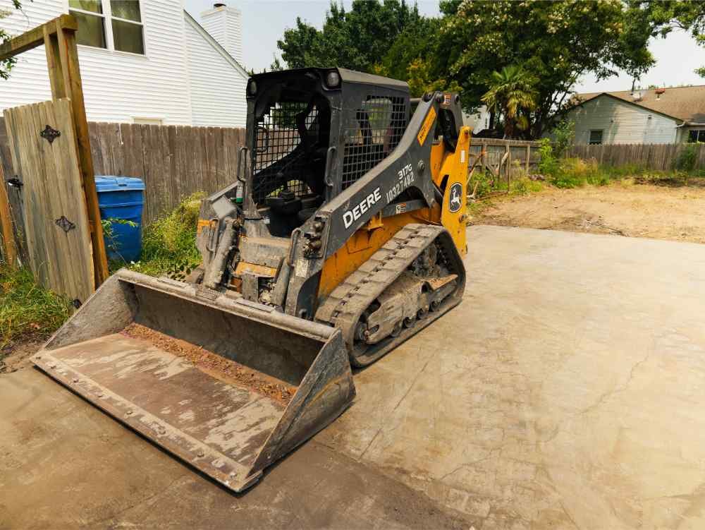 John Deere skid steer loader parked on a concrete slab during a residential demolition and site clearing project.