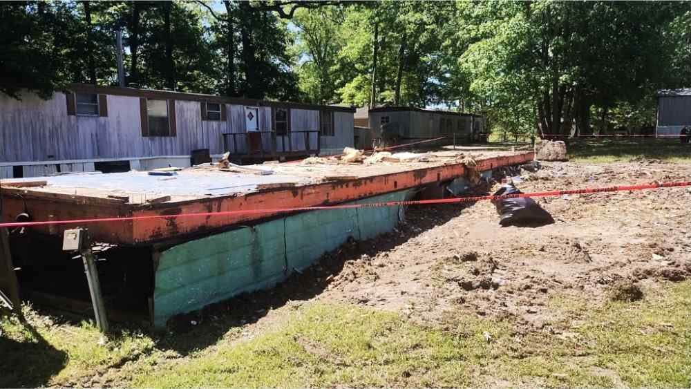 Mobile home teardown and site clearing in progress with exposed metal frame and debris.