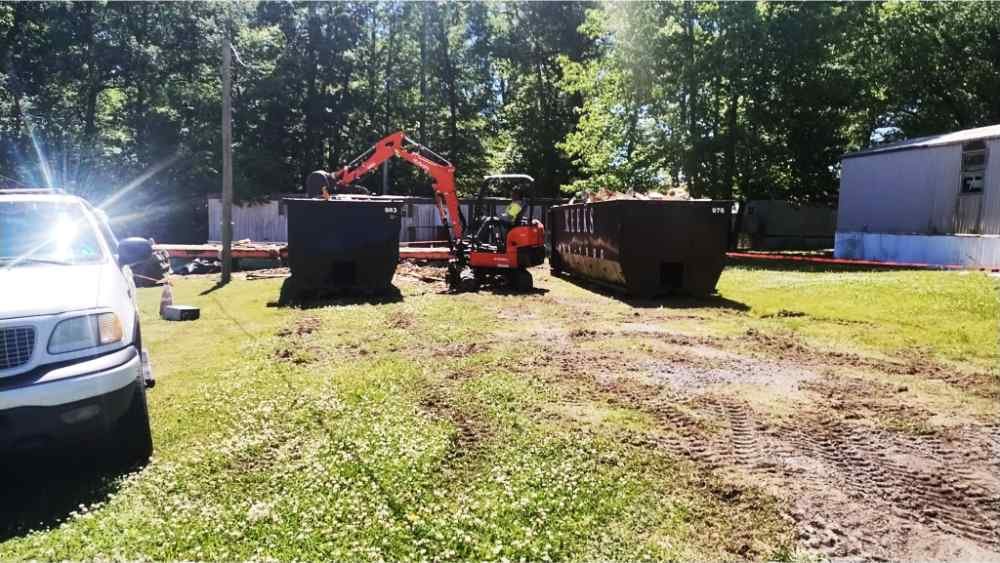 Excavator loading demolition debris into roll-off dumpsters during site clearing and teardown.
