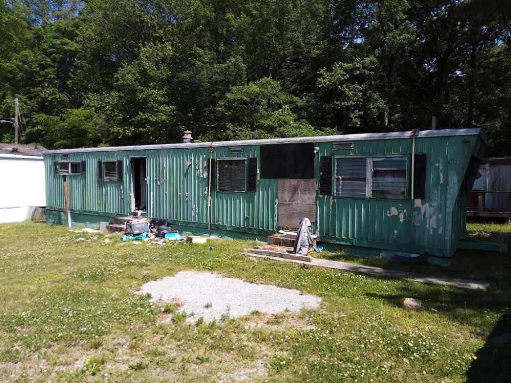 Old green mobile home slated for residential teardown and removal services.