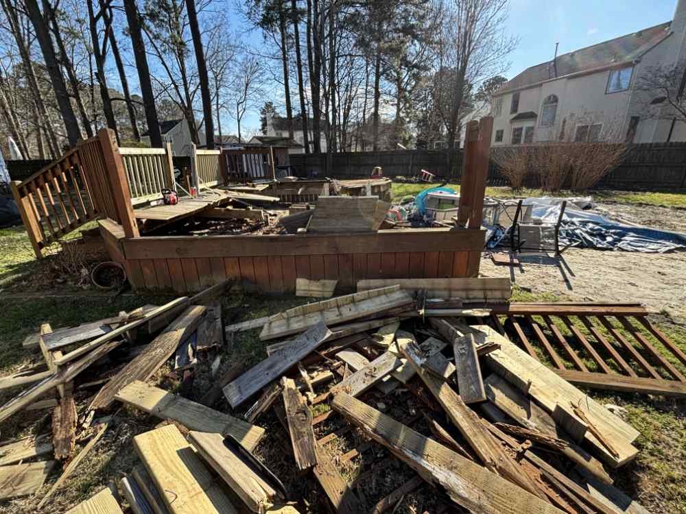 Wooden deck demolition in a residential backyard with a pile of lumber debris.