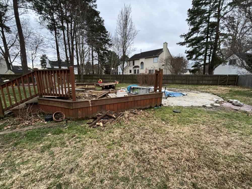 Residential backyard with a partially dismantled wooden deck and demolition debris.