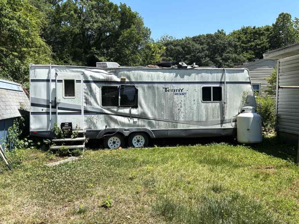 Old weathered mobile home awaiting teardown and removal services on a residential lot.