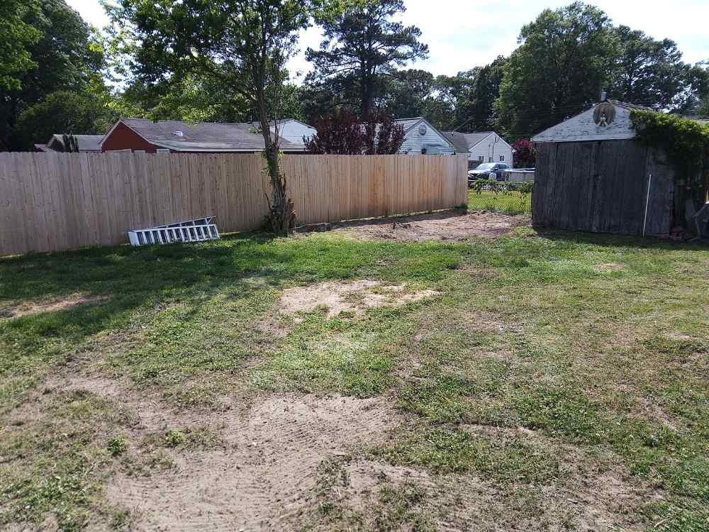 Residential backyard after shed demolition and site clearing, showing leveled ground and wooden fence.