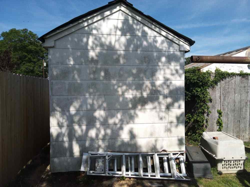 Exterior view of a small concrete block shed slated for residential demolition and site clearing.