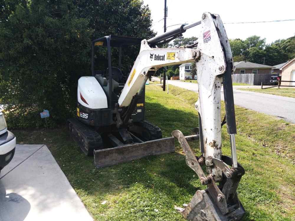 White Bobcat mini excavator parked at a residential property for site clearing and demolition services.