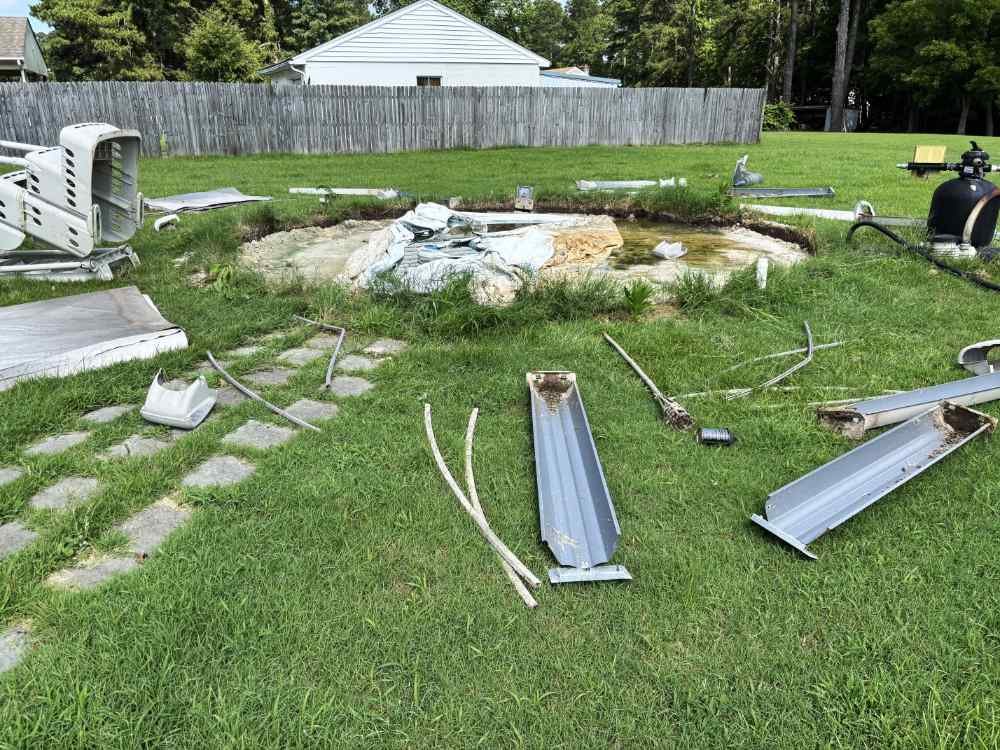 Disassembled above-ground pool parts and frame debris on grass during a residential pool removal project.