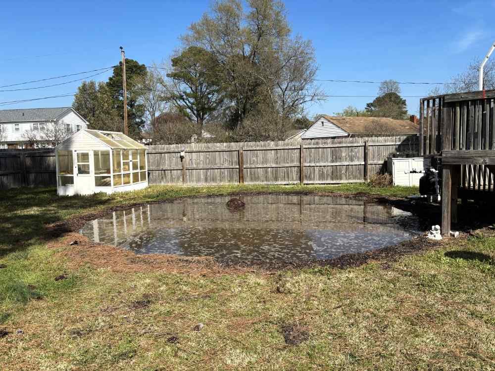 Circular flooded pit in a residential backyard following professional pool removal and site clearing.