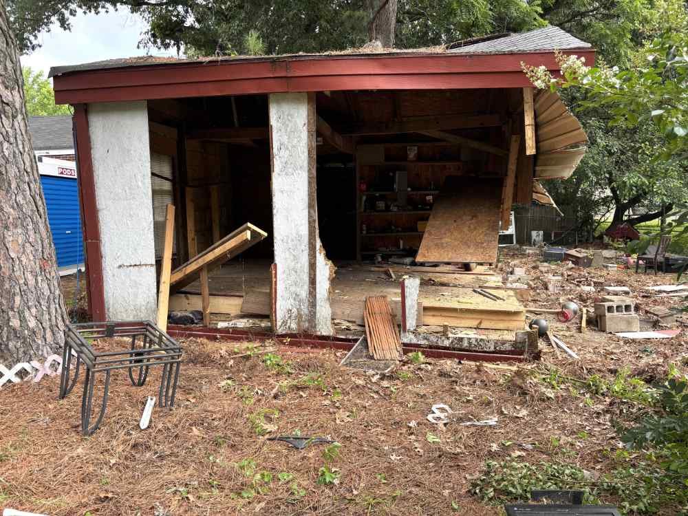 Partial shed demolition showing structural teardown and scattered debris on a residential property.